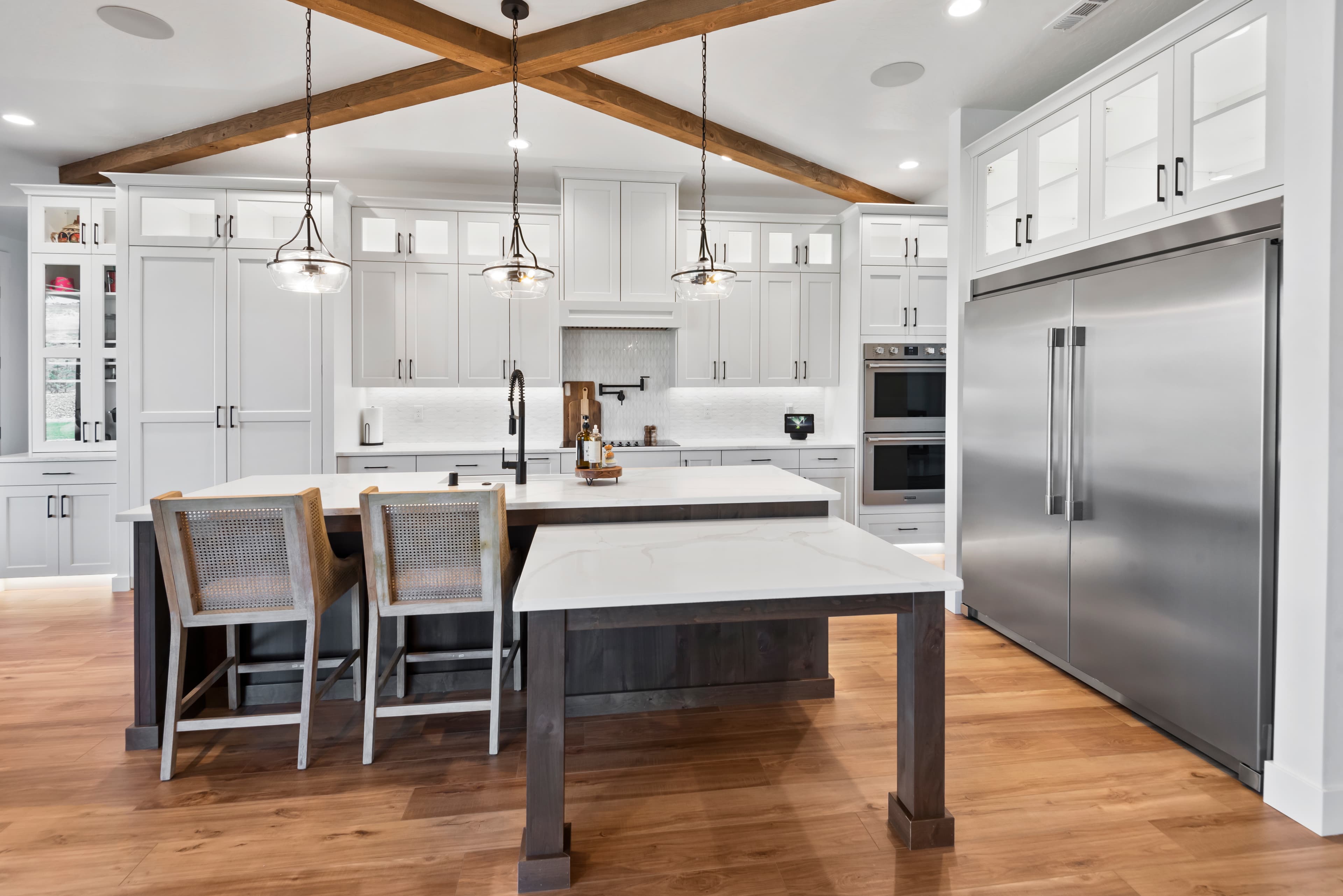 Custom white shaker kitchen with exposed wood beams and a dark wood island, built by Hill Country Cabinets